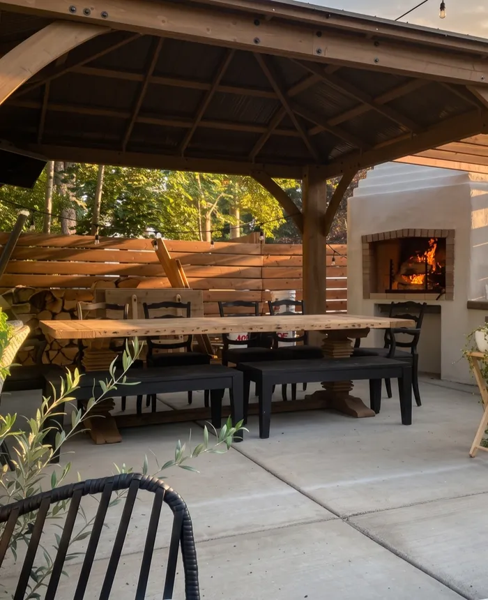 Timber pergola with a long dining table and a lit wood-fired fireplace