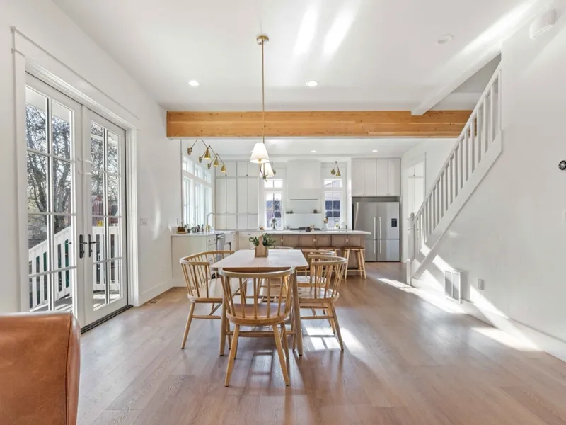 Open kitchen and dining space with an exposed wood beam, brass pendant lighting, and staircase
