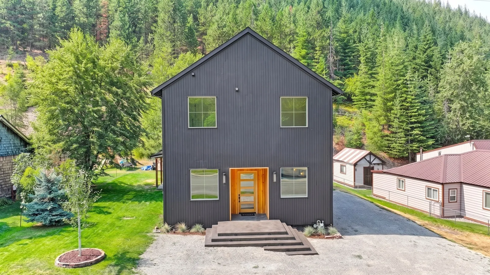Black board-and-batten custom home with a cedar entry against a forested Silver Valley hillside