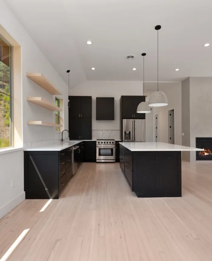 Open kitchen with black cabinetry, white quartz island, and a plaster fireplace with wood slat wall