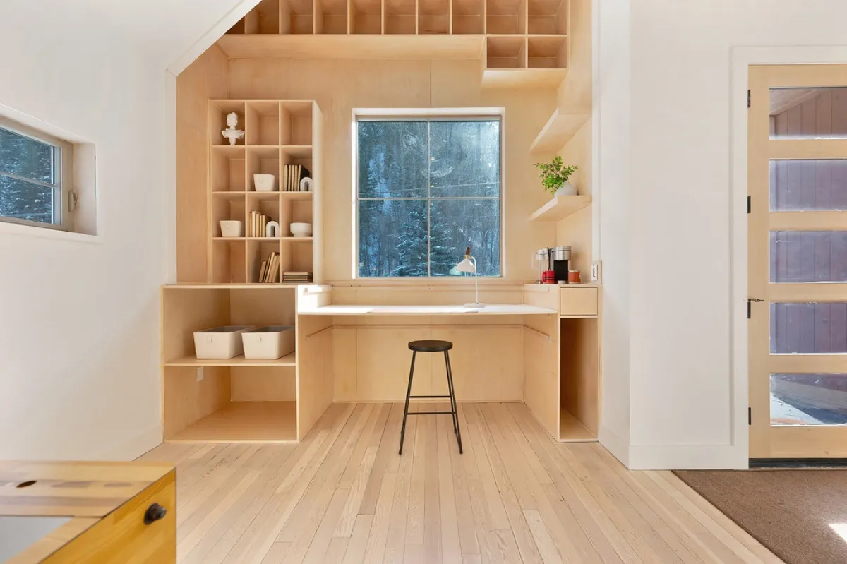 Custom built-in plywood shelving and desk nook with snow visible through the window