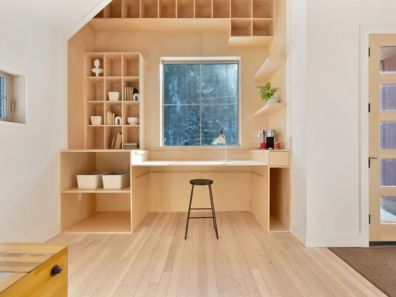 Custom built-in plywood shelving and desk nook with snow visible through the window