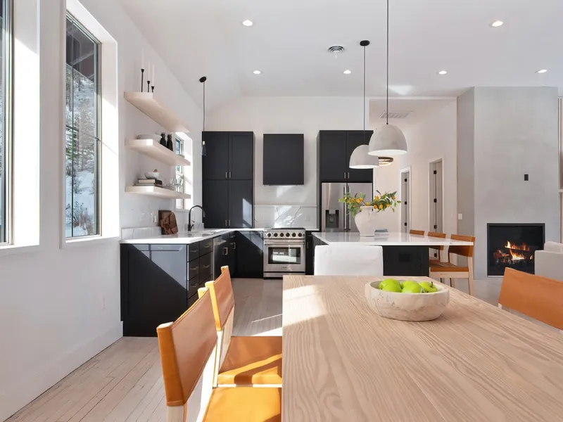 Remodeled kitchen and dining space with black cabinetry, a wood dining table, and a lit fireplace