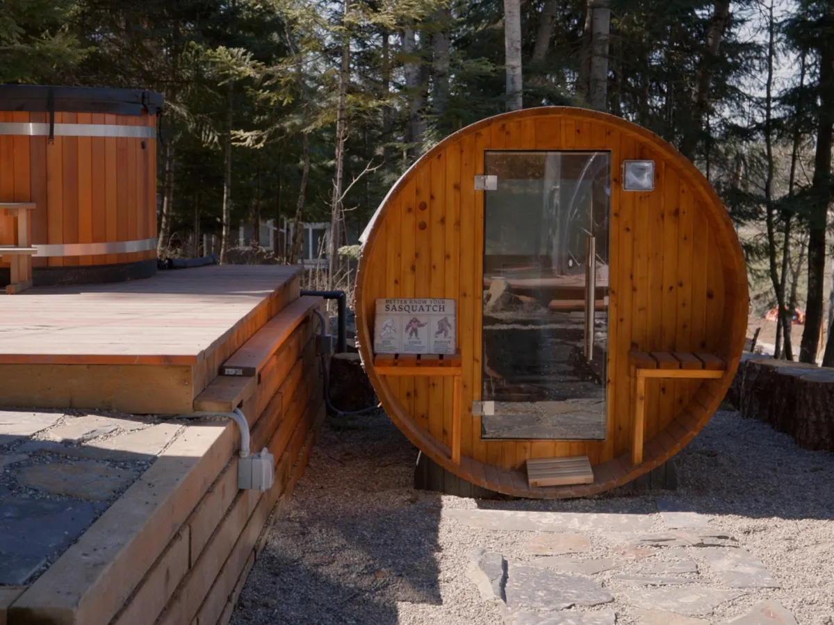 Cedar barrel sauna and round cold-plunge tub on a stone patio in summer